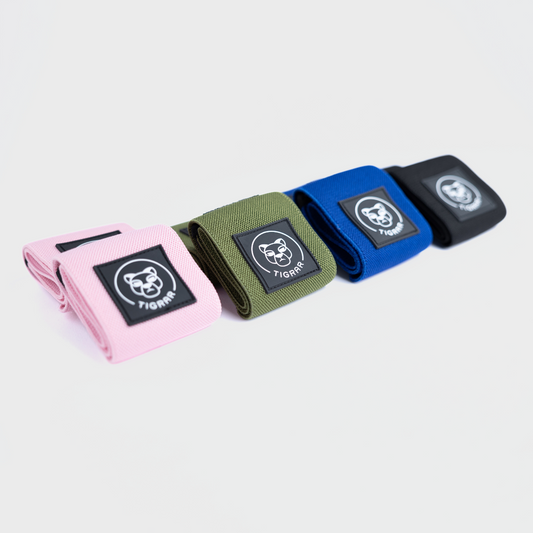 Tigrar wrist wraps in roze, groen, blauw en zwart opgesteld tegen een grijze achtergrond
