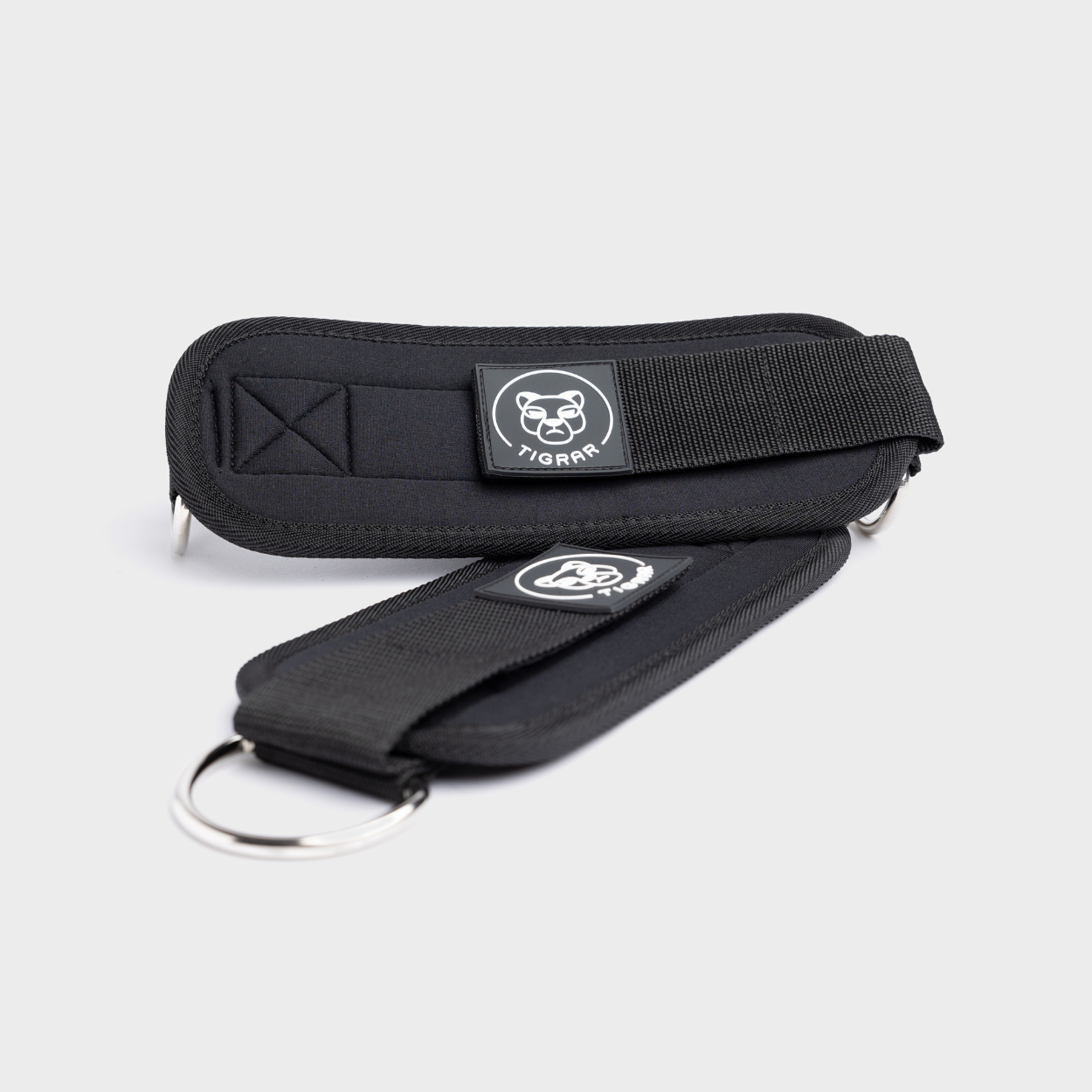 Zwarte Tigrar ankle straps met dubbele D-ring. Biedt uitstekende ondersteuning tijdens leg abductions, perfect voor het versterken van de heupspieren.