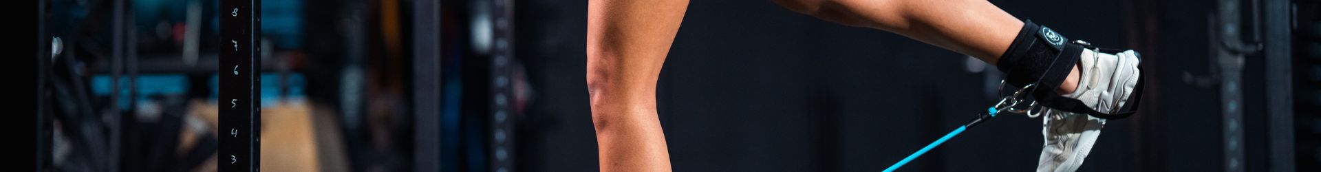 Vrouw voert een cable kickback uit met ankle straps in de gym.