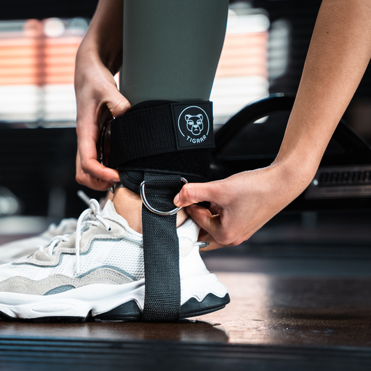 Close-up van zwarte Tigrar enkel strap gedragen om de enkel, met één hand bij de enkelband en de andere bij een bevestigingsring.