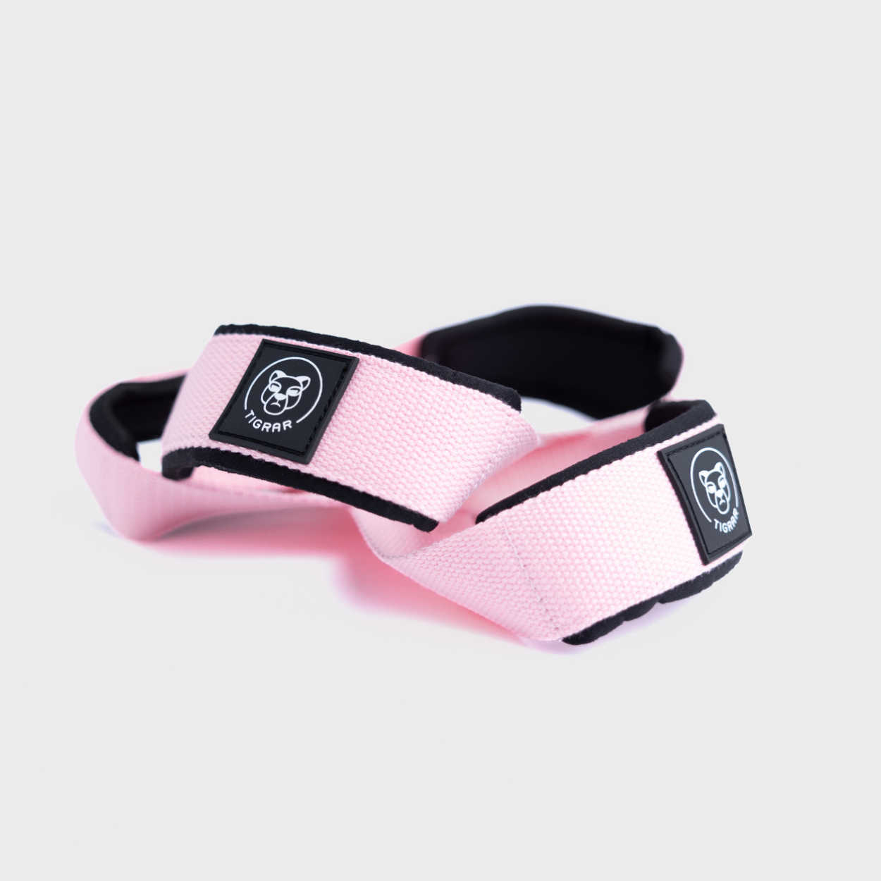 Veilige grip met Tigrar's roze Figure 8 nylon straps, ontworpen met dubbele neopreen padding. Afgebeeld op een grijze achtergrond.