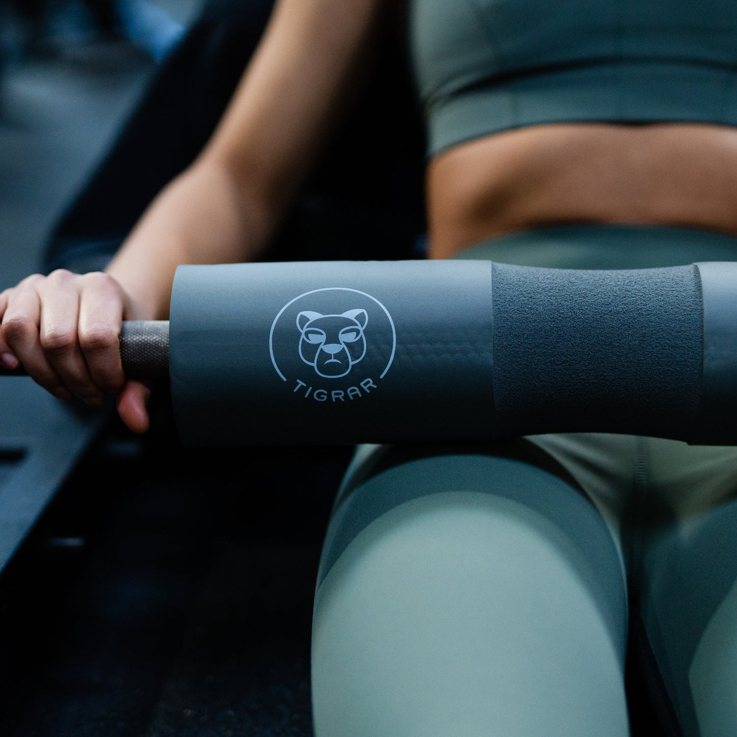 Atlete traint met een Tigrar barbell foam pad tijdens een hip thrust, fitnessapparatuur op de achtergrond
