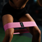 Sportster maakt een squat beweging met een roze Tigrar resistance band boven haar knieën.