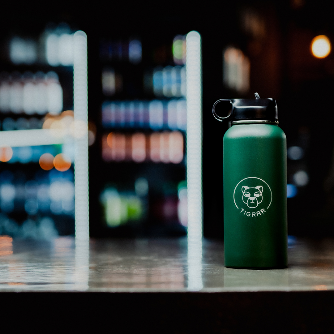 Groene milieuvriendelijke Tigrar thermosfles, prominent aanwezig op een sportschoolbar, moedigt hergebruik aan voor waterconsumptie tijdens workouts.