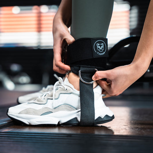Close-up van zwarte Tigrar gym ankle straps om de enkel, met stevige bevestigingsring voor krachttraining.