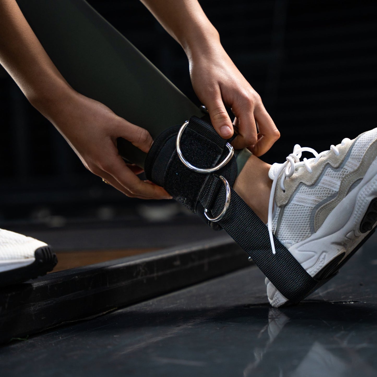 Sportvrouw demonstreert ankle strap gym tijdens een glute kickback, bevestigd aan een kabelmachine.