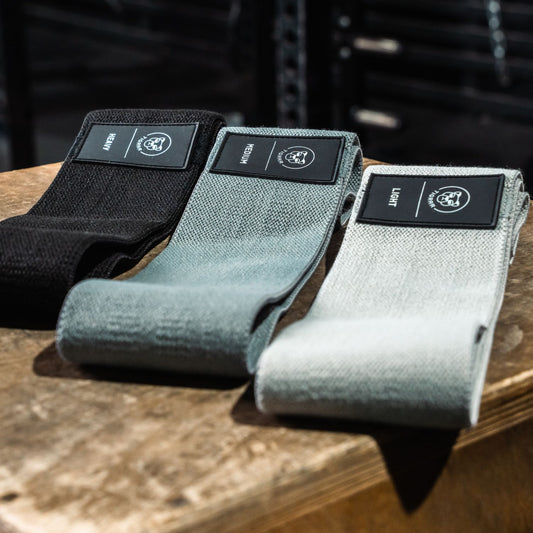 Tigrar booty bands in zwart, grijs en lichtgrijs liggen op een houten kist in een professionele gym.