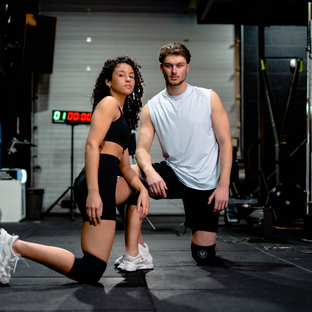Man en vrouw op één knie in de gym, beiden uitgerust met Tigrar knee sleeves.