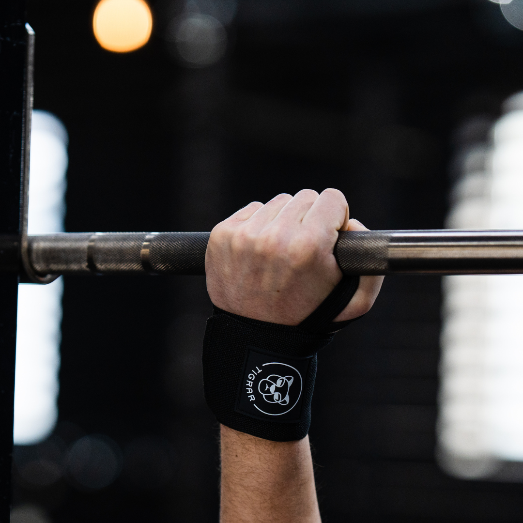 Close-up van een arm tijdens de bench press met een Tigrar wrist strap om de pols gewikkeld.