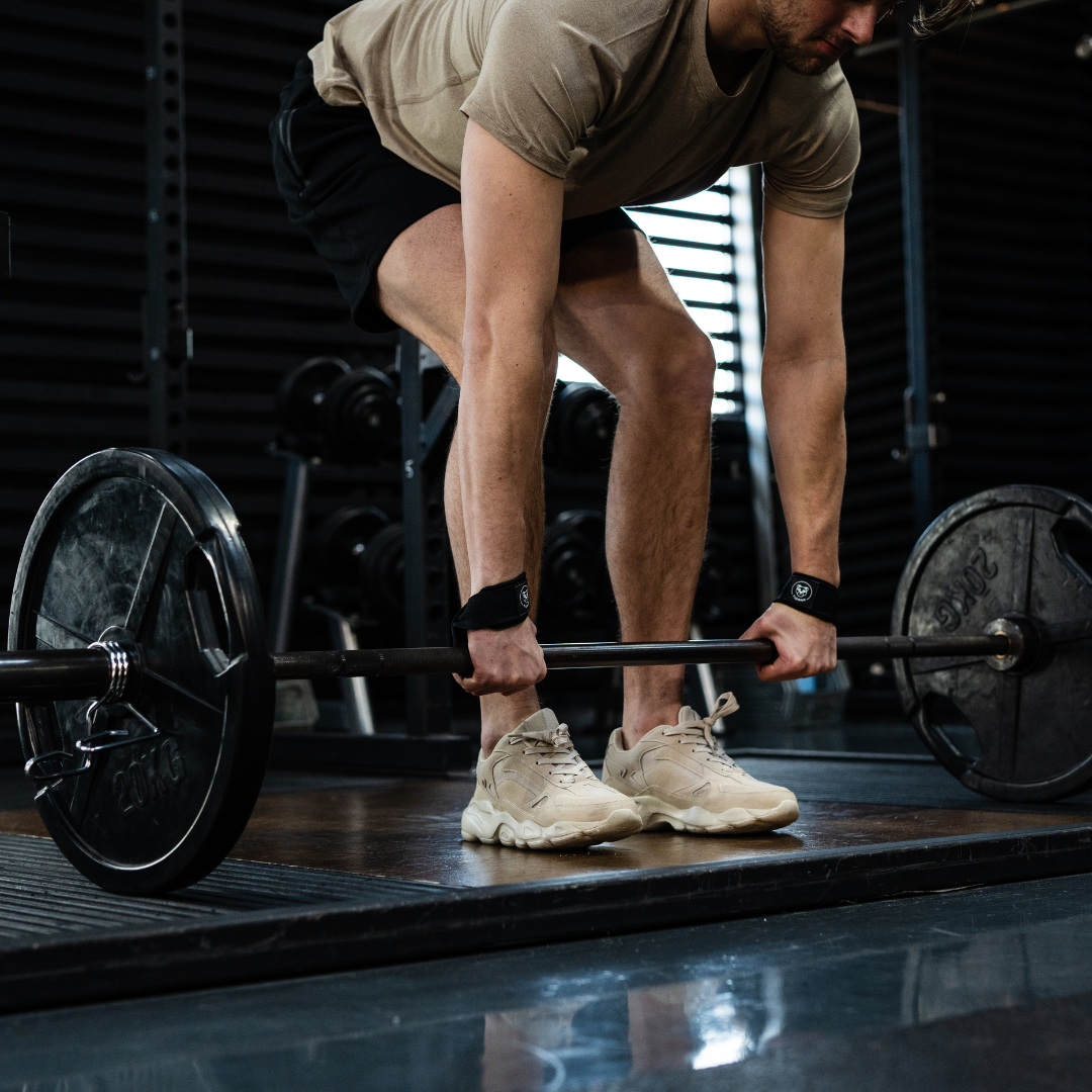 Man buigt voorover om zijn lifting straps correct aan te brengen voor de deadlift-oefening met de stang.