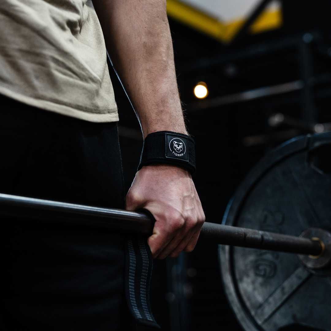 Close-up van atleet's hand die een zwarte Tigrar lifting strap vasthoudt tijdens een deadlift, benadrukt gripstabiliteit.