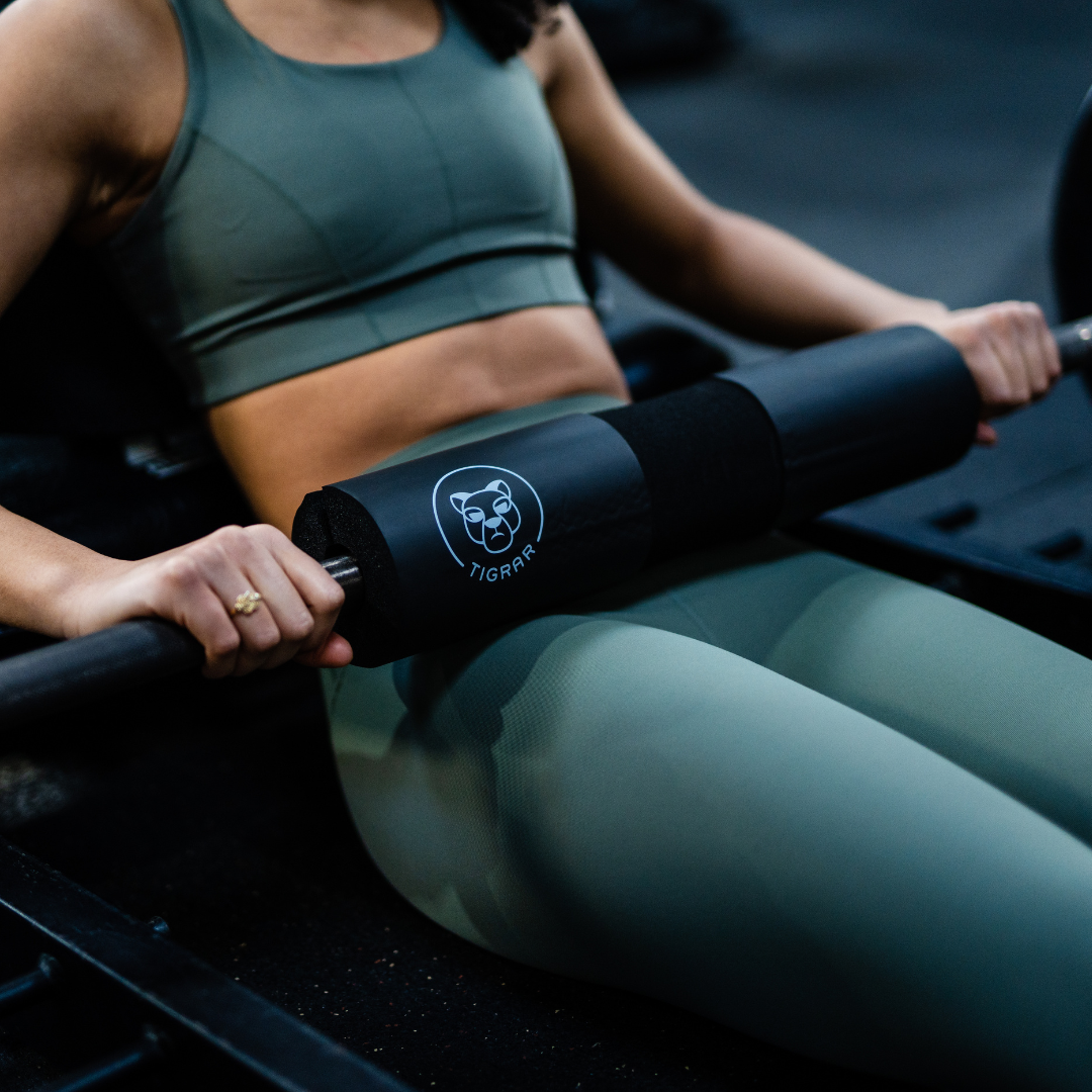 Jonge vrouw doet een hip thrust in de gym, close-up van barbell stang met Tigrar bar pad op haar heupen.