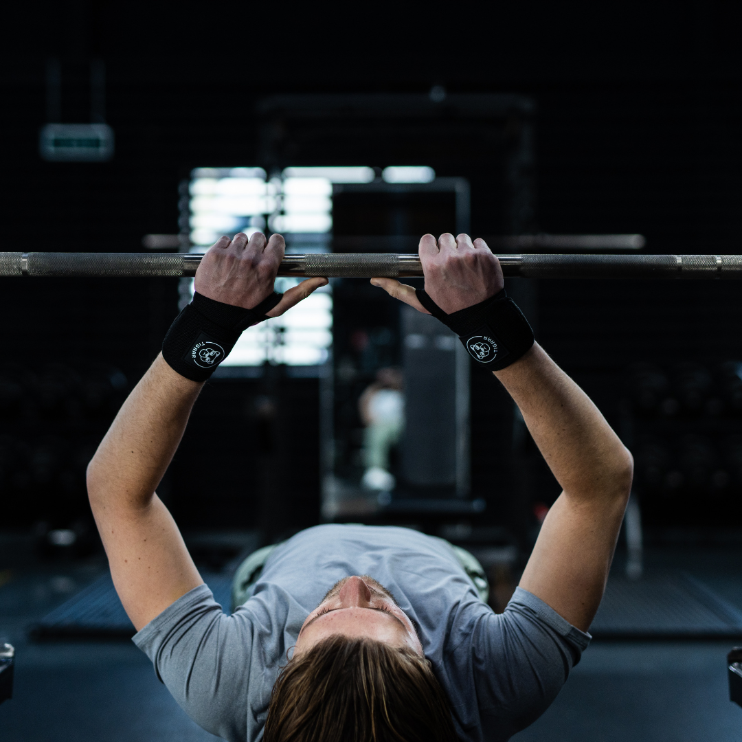 Man in bench press positie met Tigrar wrist wraps, gereed om de stang vast te pakken.