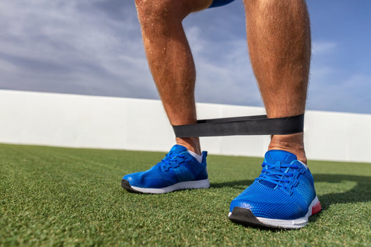Close-up van een sportieve man die buiten een banded monsterwalk uitvoert op gras, met een weerstandsband rond zijn scheenbenen en focus op de voetpositie en kniebuiging