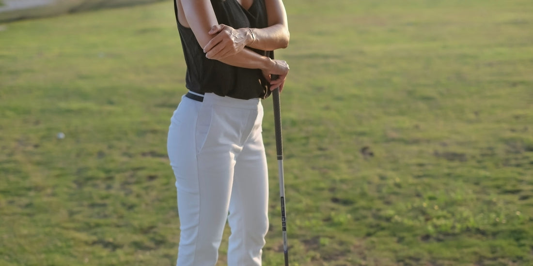 Vrouw staat op de golfbaan en houd haar elleboog vast omdat ze last heeft van een golfarm