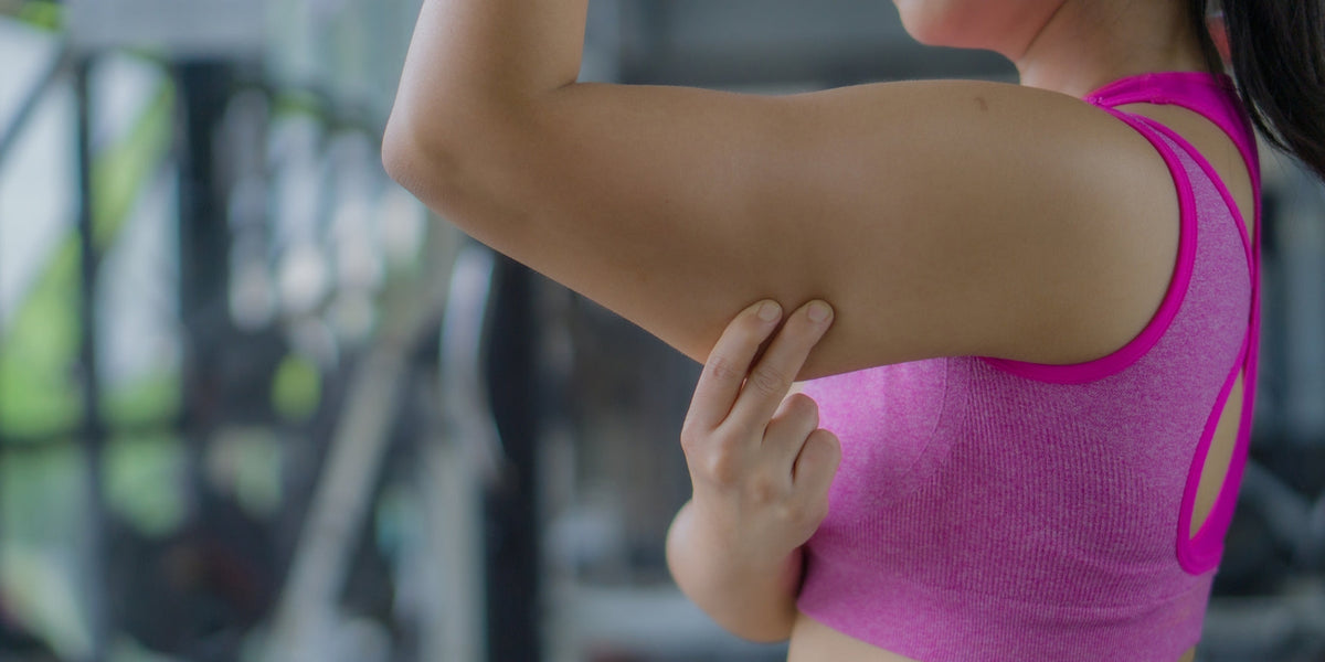 sportieve vrouw toont haar arm en pakt met haar hand de onderkant van haar bovenarm vast om haar kipfilet arm te tonen.