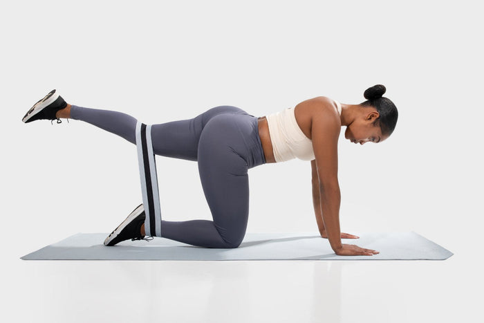 Sportieve vrouw gebruikt een kleine weerstandsband tijdens haar glute bridge oefening.