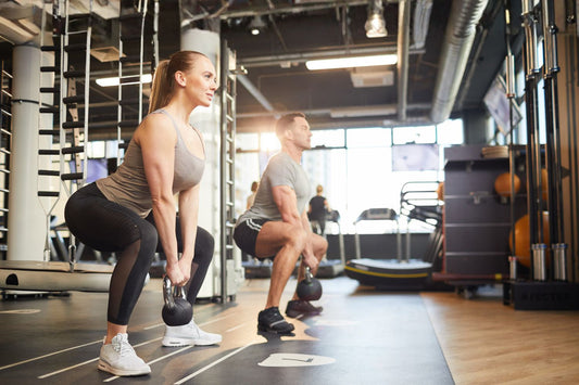 Man en vrouw voeren samen een kettlebell squat uit in de sportschool voor sterke benen en goede squat techniek