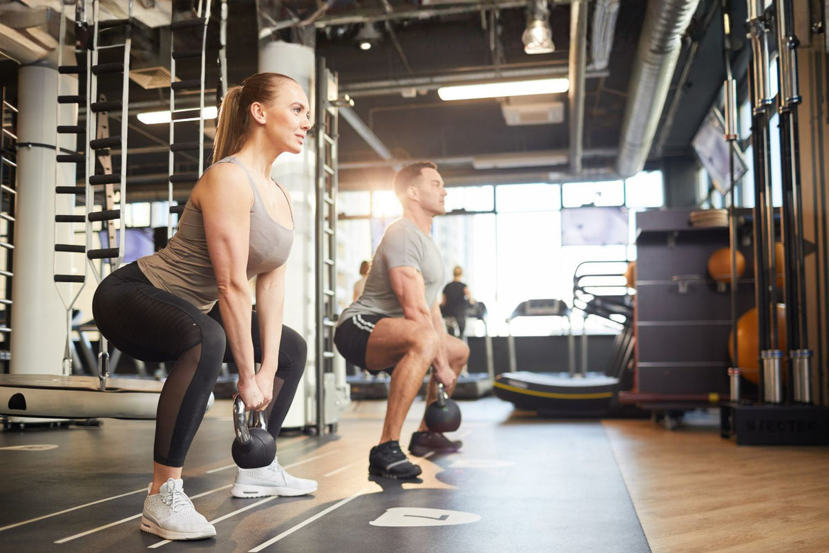 Man en vrouw voeren samen een kettlebell squat uit in de sportschool voor sterke benen en goede squat techniek