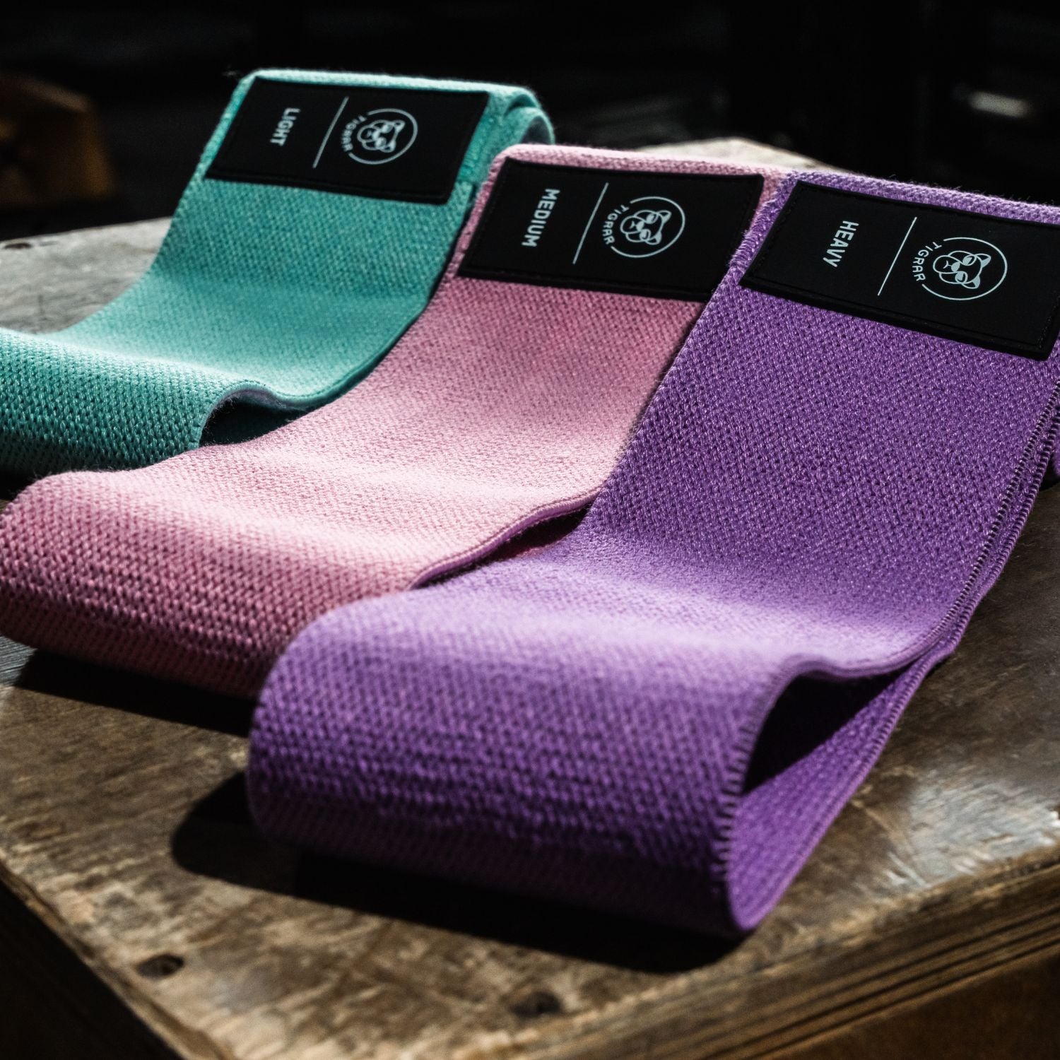 light, medium en heavy booty bands in de kleuren mint, roze en paars liggen op een plyo box in de gym