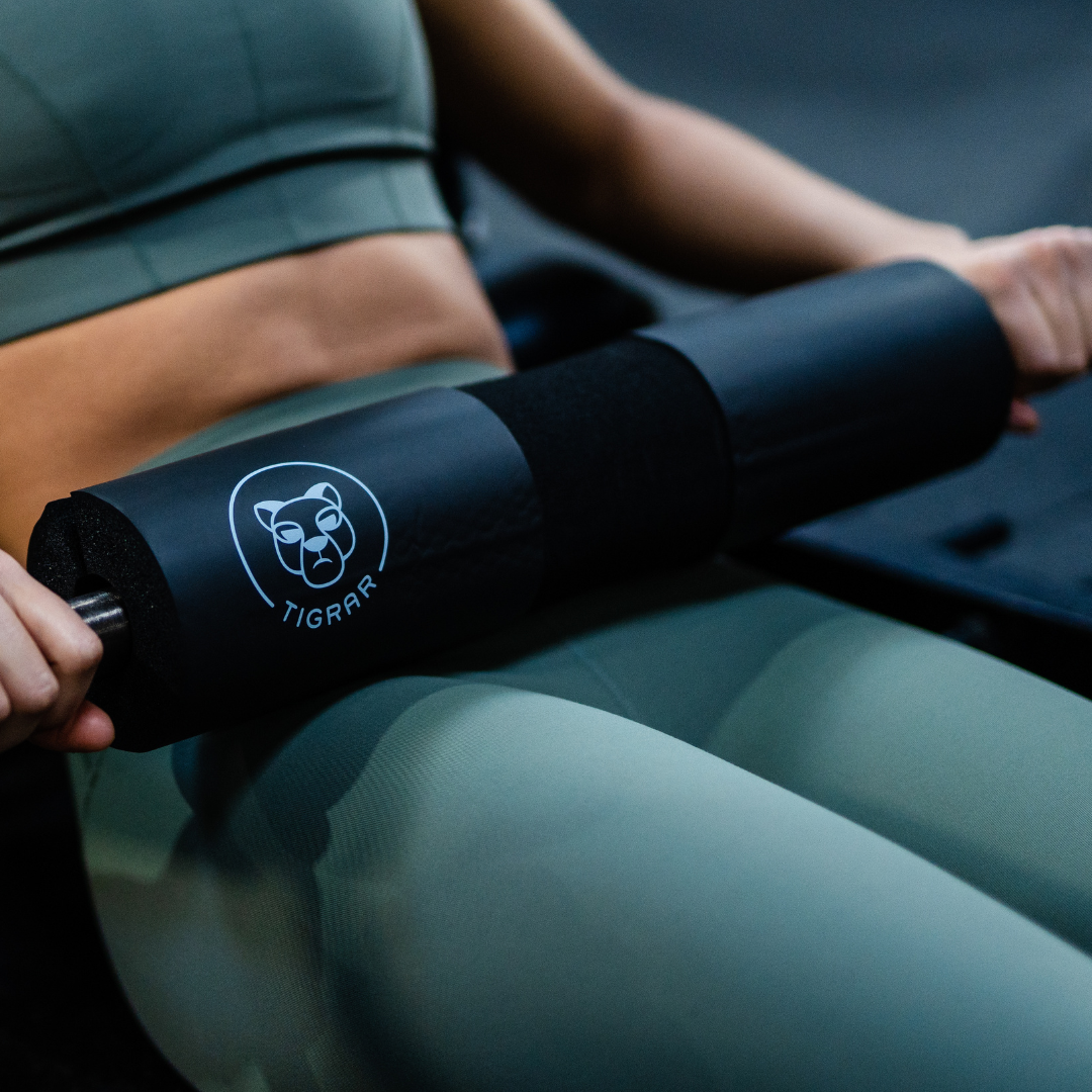 Atlete gebruikt een zwarte Tigrar barbell foam pad bij een hip thrust oefening, detailrijk in beeld gebracht.