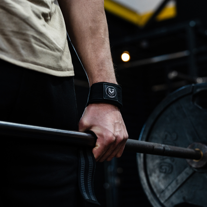 Close-up van een arm met een Tigrar weight lifting strap tijdens een deadlift-oefening met de stang op heuphoogte.