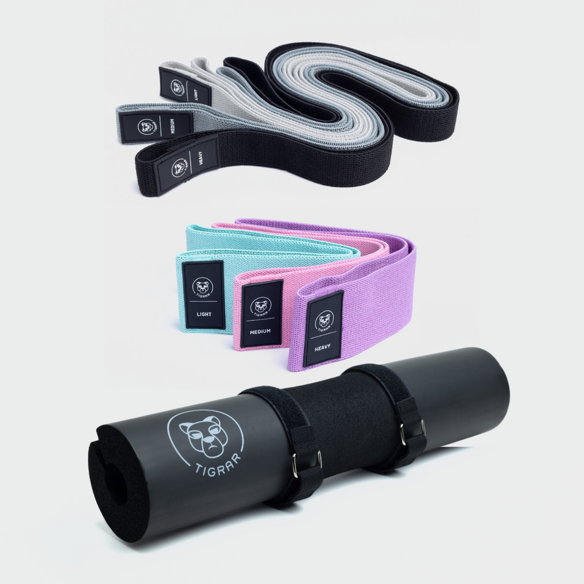 Set van Tigrar: drie lange weerstandsbanden in zwart, grijs, lichtgrijs, drie korte in mint, roze, paars en een zwarte barbell pad. Alle accessoires op een grijze achtergrond