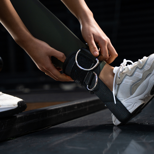 Close-up van een sportieve dame die een Tigrar enkel strap met zachte padding en kickback strap onder de hiel vasthoudt.
