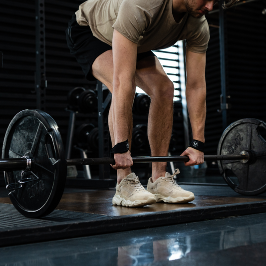 Man buigt voorover om zijn weight lifting straps correct aan te brengen voor de deadlift-oefening met de stang.